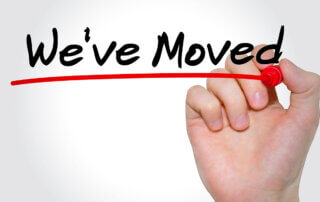 Image of hand drawing on clear screen. The text that is written on the screen says "We've Moved"