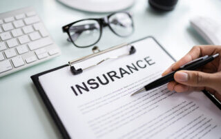 a clipboard with documents showing the words "Insurance" on the front page