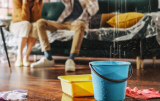 renters in the backround sitting on a couch, the foreground shows buckets catching water drops falling from the ceiling
